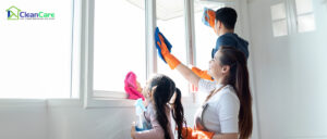 A family of three wiping windows together